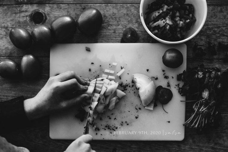 Black and white photo of hands making salsa with tomatoes and onions
