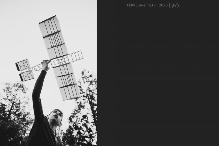 black and white photo of boy lifting a homemade airplane in the air