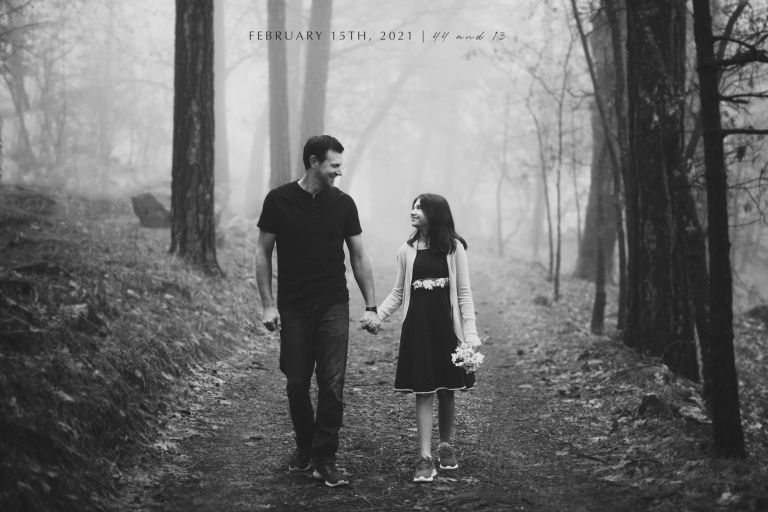 father and daughter walking hand in hand down a path in the woods black and white